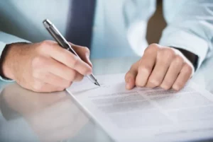 Homme en chemise signant un document administratif officiel avec un stylo-plume.