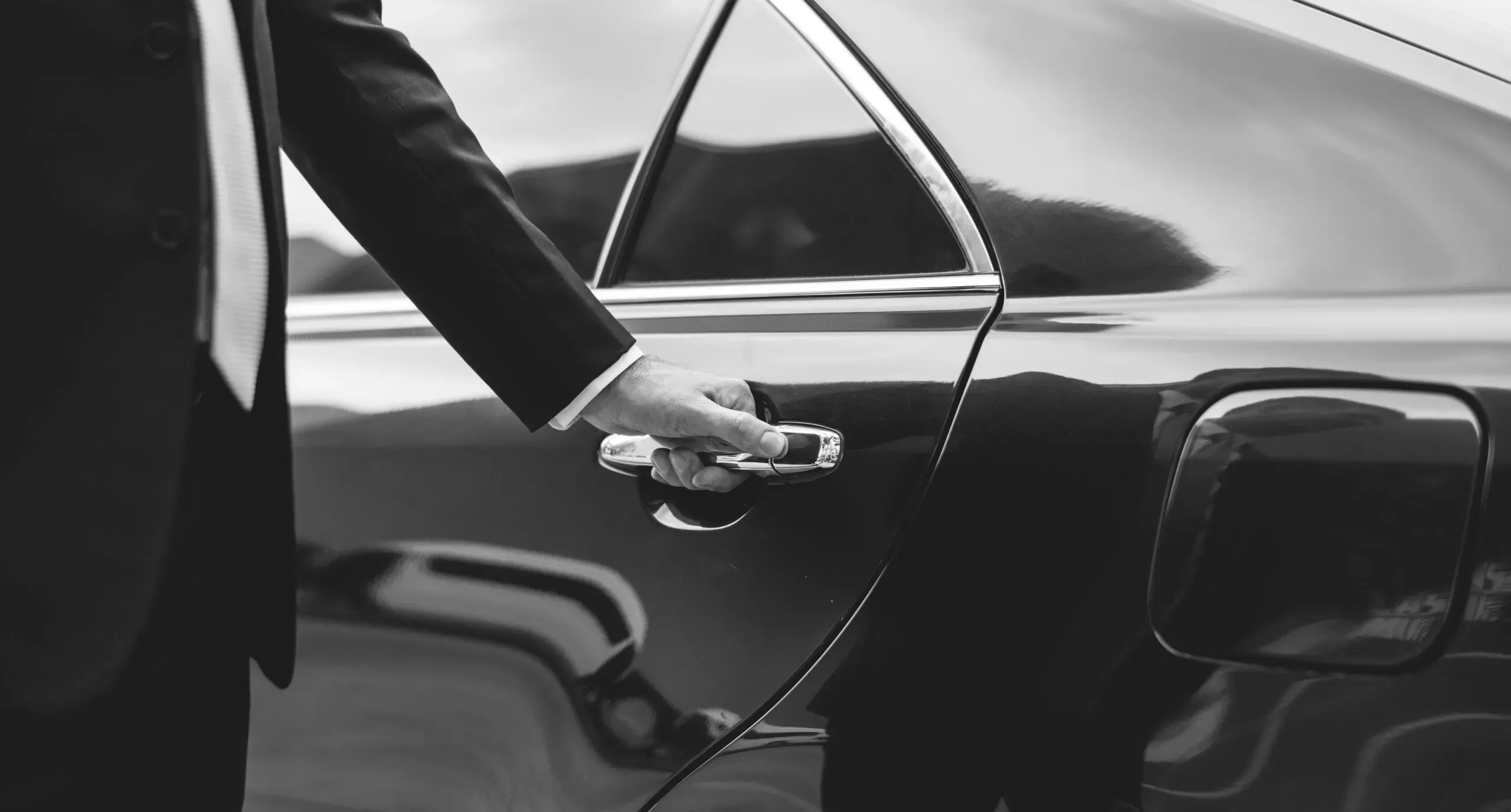 Chauffeur privé en costume ouvrant la portière d'une voiture de luxe noire.
