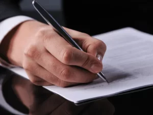 Gros plan sur la main d'un homme signant un contrat d'obsèques avec un stylo.