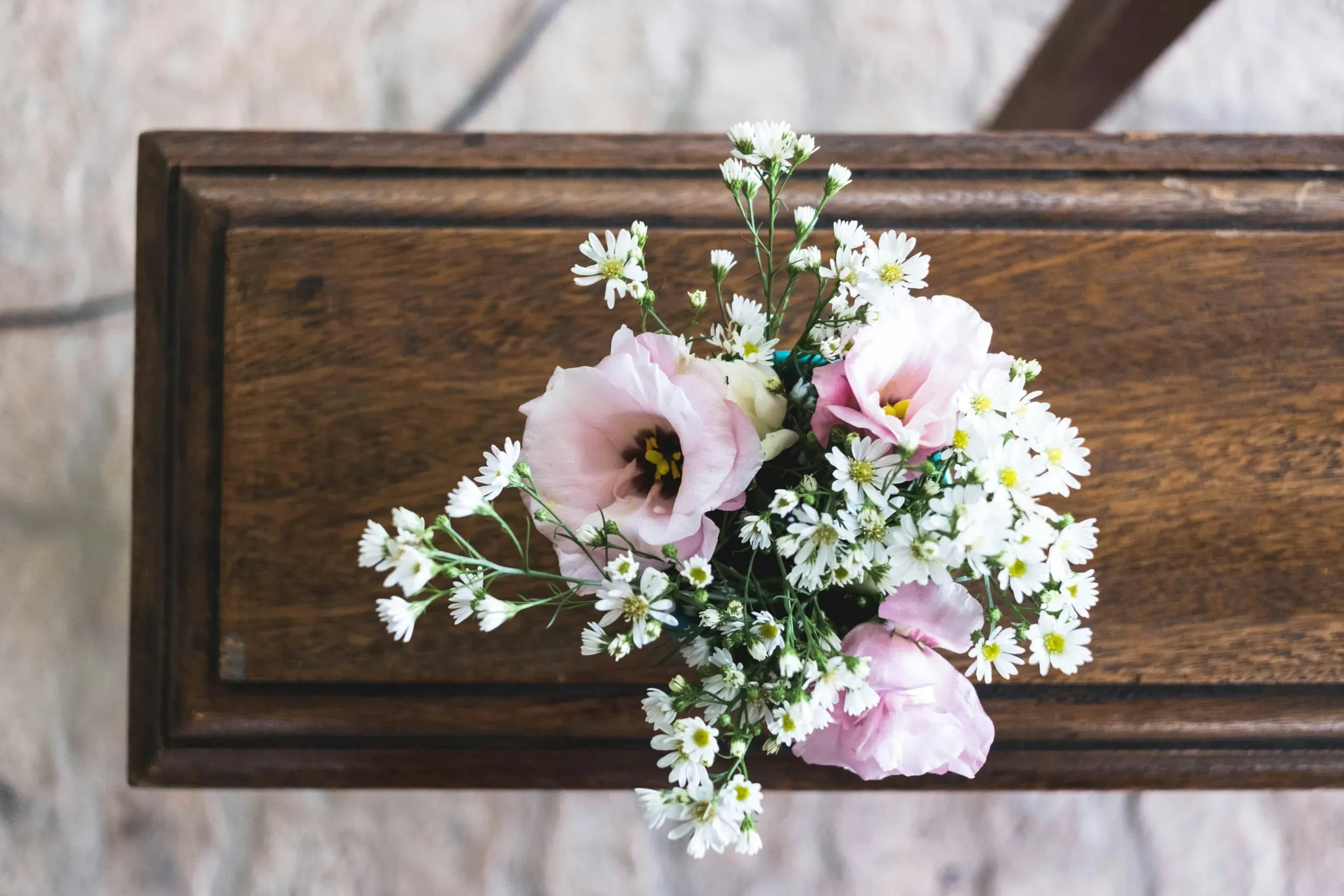 Petit bouquet de fleurs roses et blanches posé sur un meuble en bois massif.