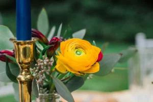Bougie bleue et composition florale avec ranoncule jaune sur chandelier doré.