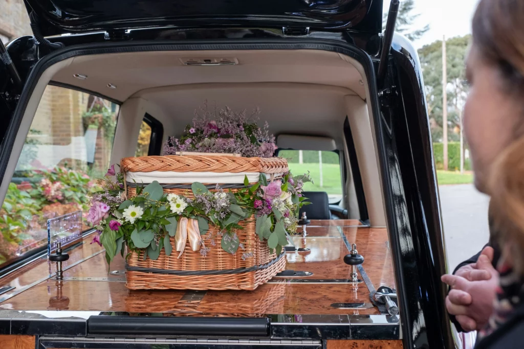 Cercueil en osier tressé garni de fleurs champêtres dans un corbillard.