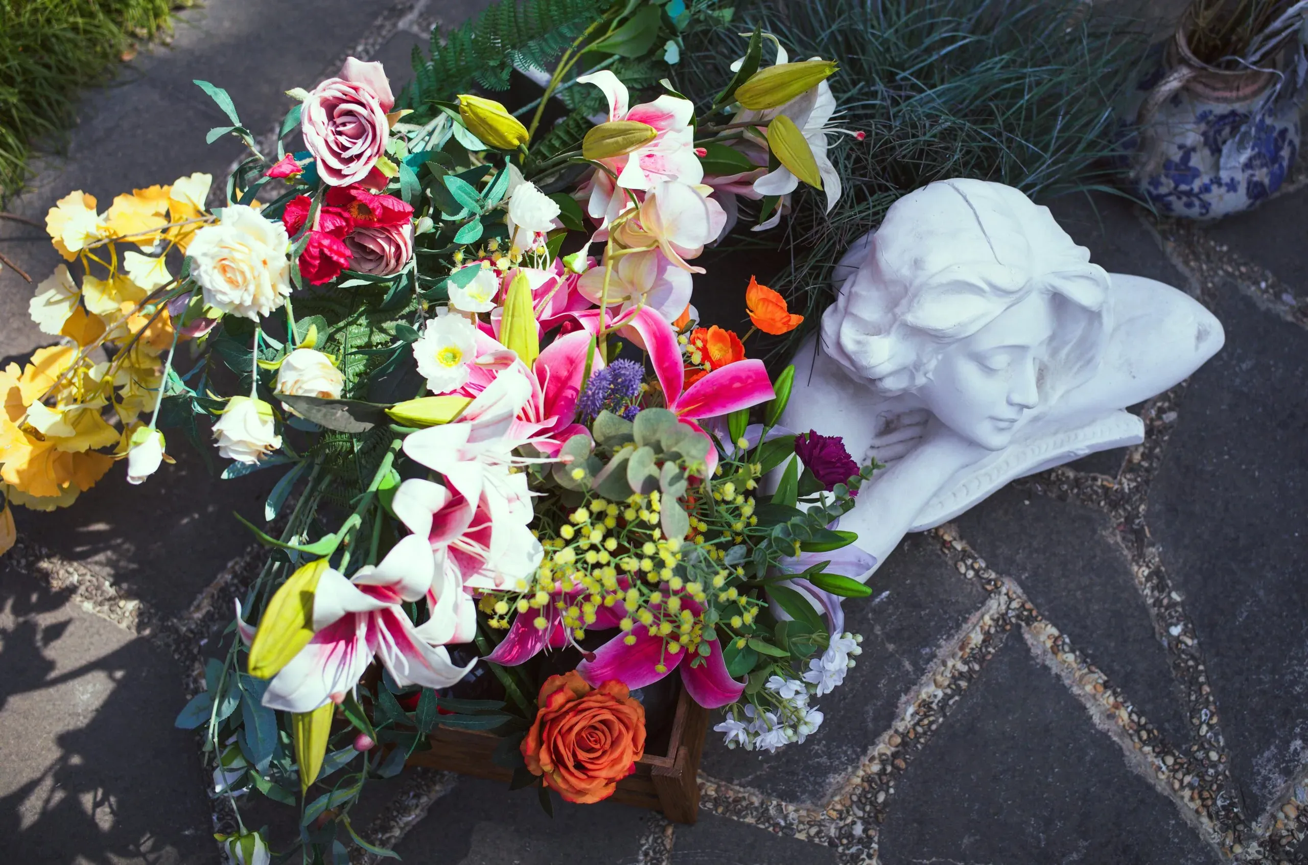 Bouquet de fleurs de deuil colorées posé près d'une statue d'ange dans un cimetière.