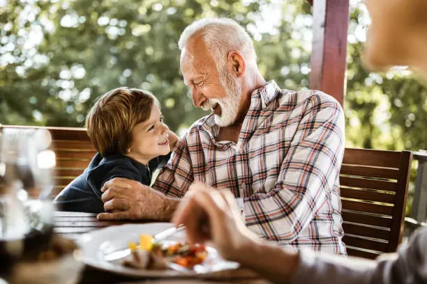 Grand-père souriant partageant un moment de complicité avec son petit-fils en extérieur.