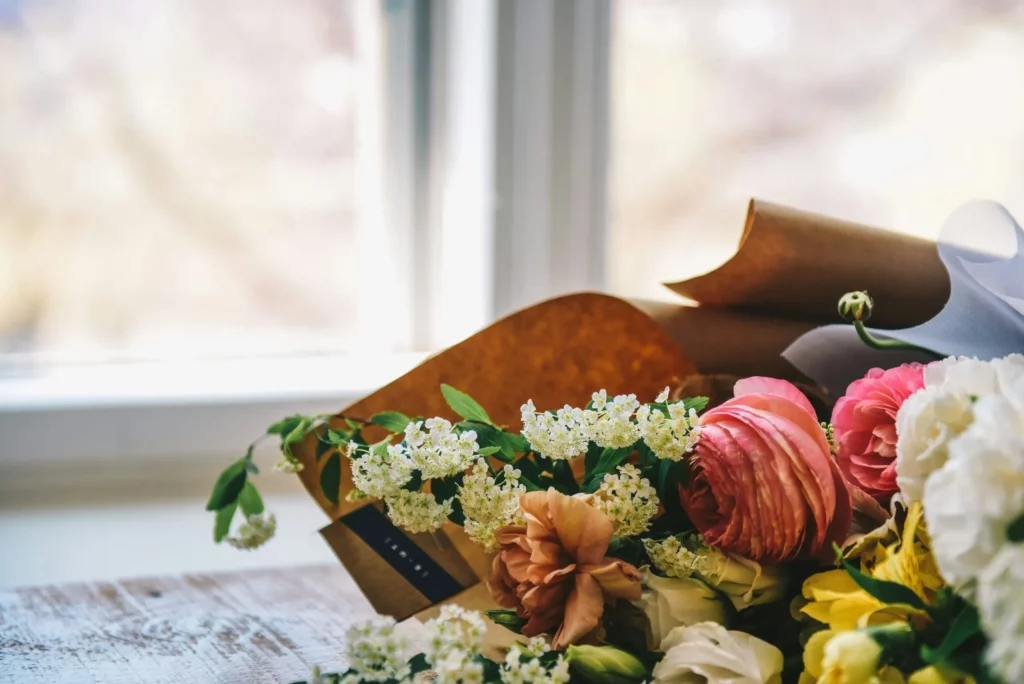 Bouquet de fleurs fraîches enveloppé de papier kraft posé sur une table en bois.