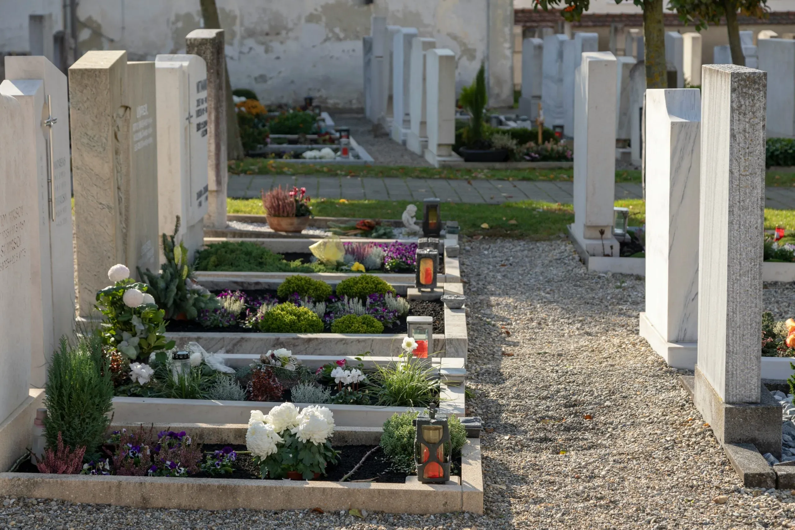 Tombes fleuries avec des lanternes le long d'une allée de cimetière.